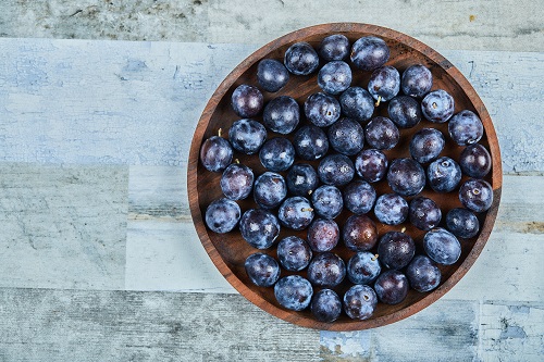 Garden plums in a plate on a blue background